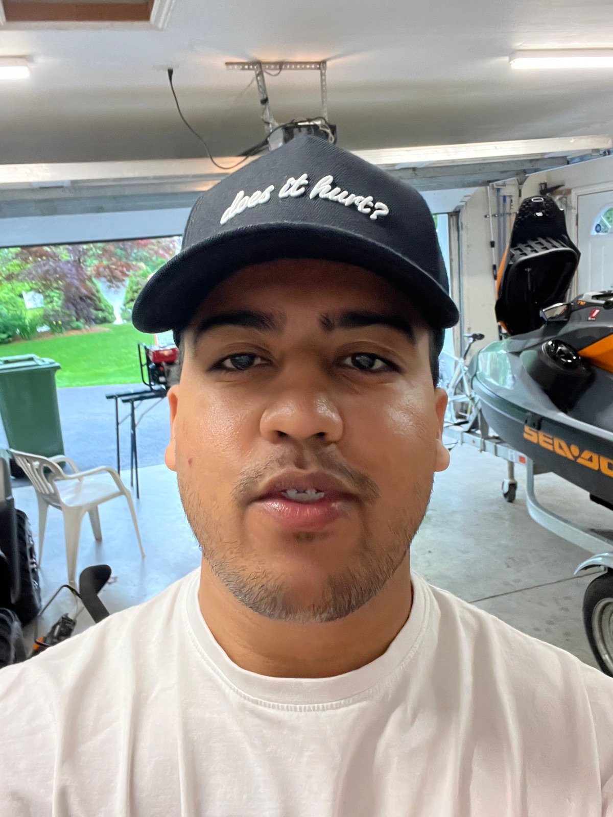 Selfie in the garage wearing a script-embroidered cap, Sea-Doo on the trailer behind